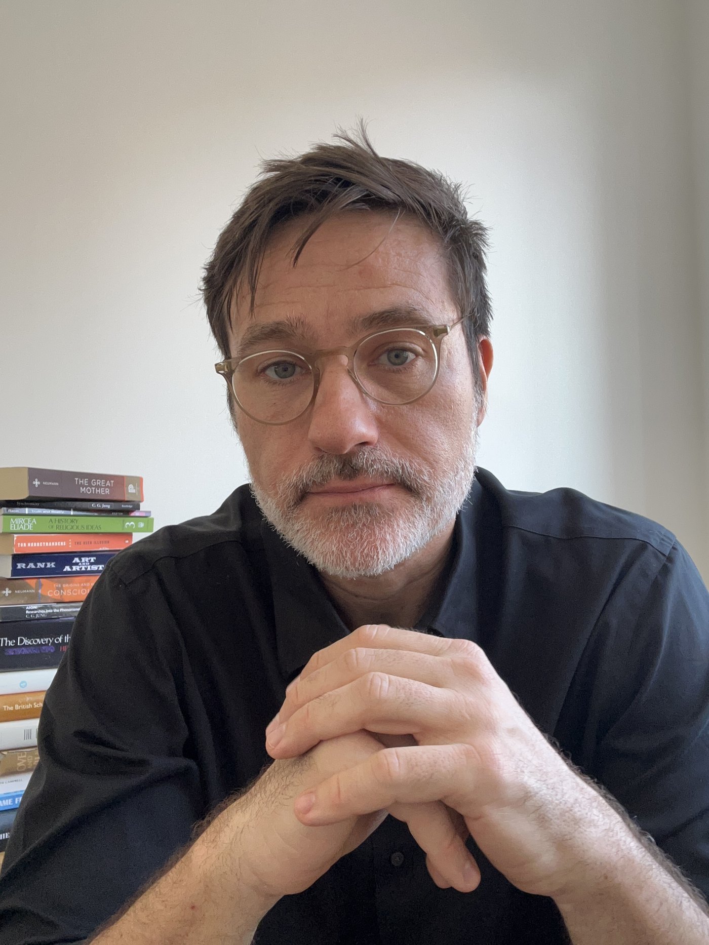 Portrait of Roberto Kilciauskas, seated, hands clasped, with a stack of psychology books behind him.